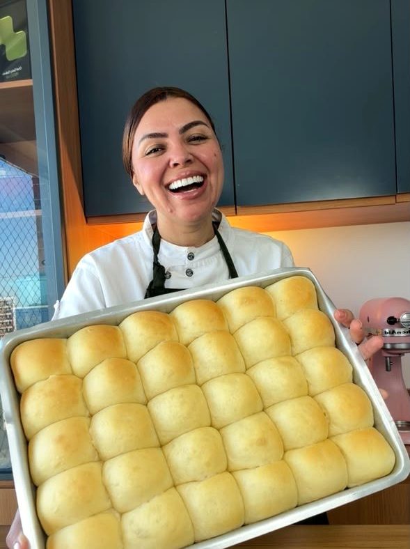 Chef Geicy Galindo segurando uma bandeja de pãezinhos dourados